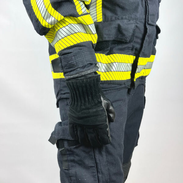 Schwarze, kurze Feuerwehrhandschuhe von Penkert, getragen an der rechten Hand einer Person in Feuerwehrschutzkleidung.