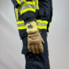 Ein Feuerwehrmann trägt Penkert FireDevil 911 X-treme kurze Handschuhe und steht mit ausgestrecktem rechten Arm, wobei das gelbe Bündchen und die reflektierenden Streifen an der Schutzkleidung deutlich sichtbar sind.