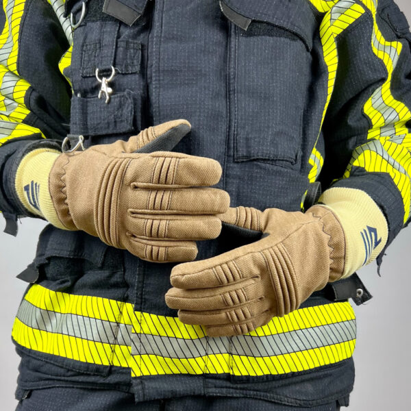 in Feuerwehrmann steht mit Penkert FireDevil 911 X-treme kurzen Handschuhen und verschränkten Armen, die reflektierenden Streifen der Schutzkleidung und das gelbe Bündchen mit dem blauen Logo sind sichtbar.