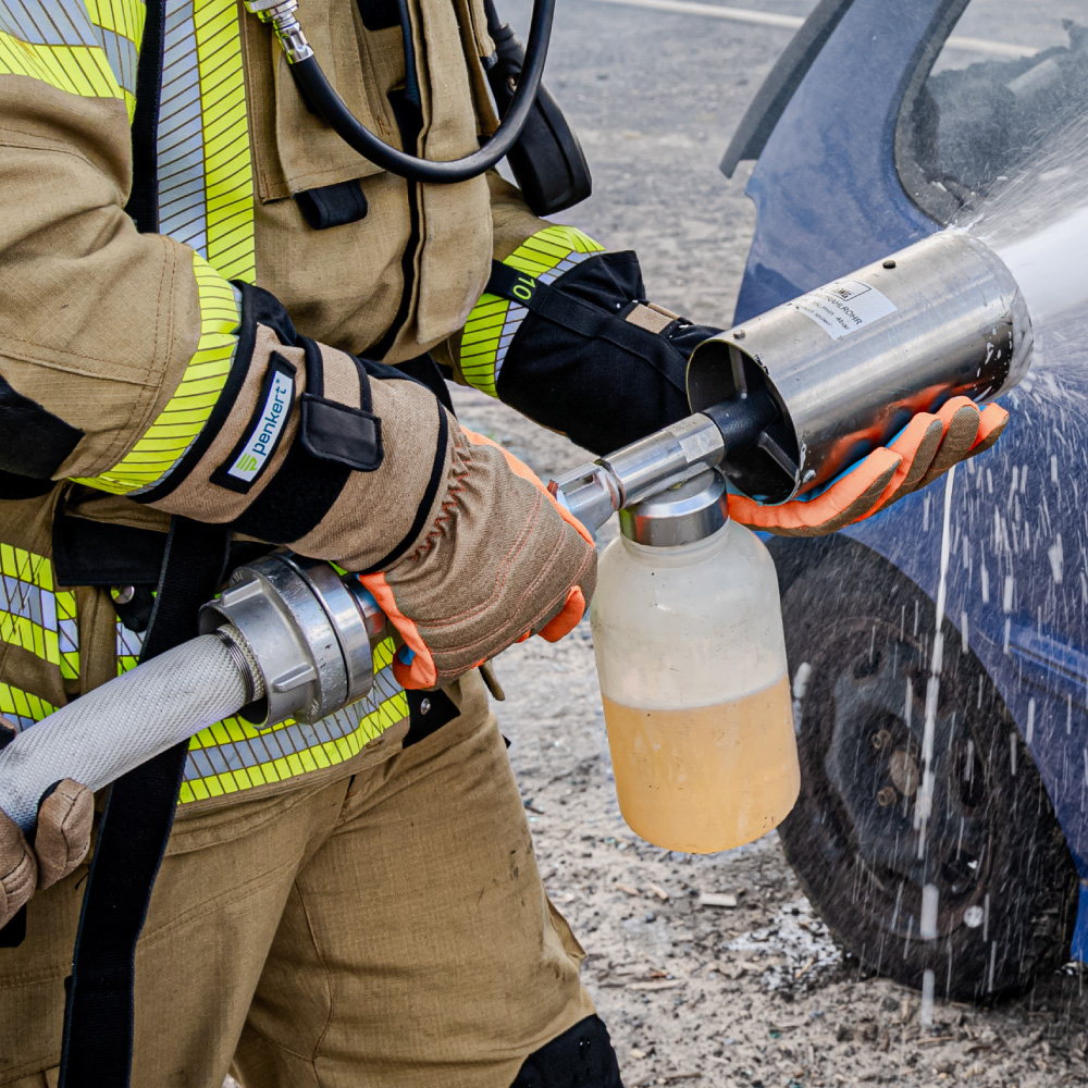 Nahaufnahme eines Feuerwehrmanns im Einsatz, der Penkert HyPA-Grip Handschuhe trägt und ein Feuerwehrgerät bedient, wobei die orangen und grauen Materialien der Handschuhe gut sichtbar sind.