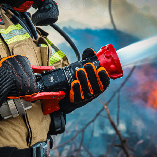 Feuerwehrmann im Einsatz trägt Penkert New Dimension 3.0 Handschuhe, hält einen Feuerwehrschlauch während des Löschvorgangs, schwarzes und orangefarbenes Design.