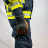 Seitliche Ansicht eines Feuerwehrmanns in Schutzausrüstung mit Penkert New Dimension 3.0 Feuerwehrhandschuhen, schwarzes und orangefarbenes Design mit kurzem Stulpen.