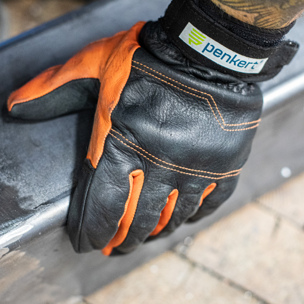 Ein Handschuh von Penkert greift ein Metallteil, wobei die strapazierfähige Lederoberfläche und die markante Naht erkennbar sind.