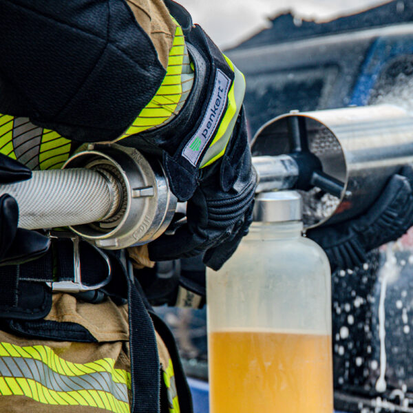 Feuerwehrkraft in voller Schutzkleidung verbindet einen Feuerwehrschlauch, während sie lange Schutzhandschuhe mit reflektierenden Streifen und Penkert-Logo trägt.