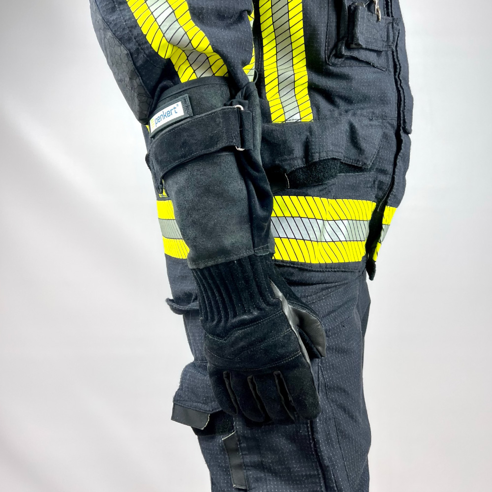 Seitliche Ansicht eines Feuerwehrmanns in kompletter Schutzausrüstung, trägt schwarze Penkert FireGrip 3.0 Feuerwehrhandschuhe mit langem Stulpen. Die reflektierenden Streifen der Schutzkleidung sind deutlich sichtbar und betonen die professionelle Ausrüstung.