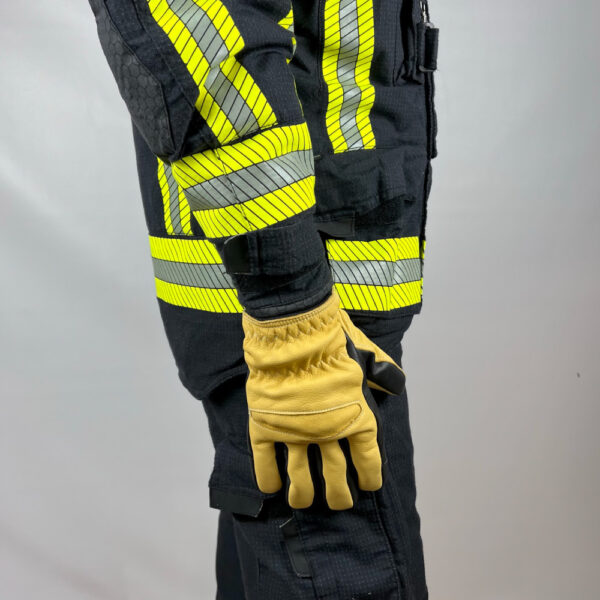 Feuerwehrhandschuh Penkert Elk Defender 3.0 in Schwarz und Beige, getragen auf einer Feuerwehrschutzjacke, die seitlich gezeigt wird, um die reflektierenden Streifen und den Handschuh in voller Länge zu präsentieren.